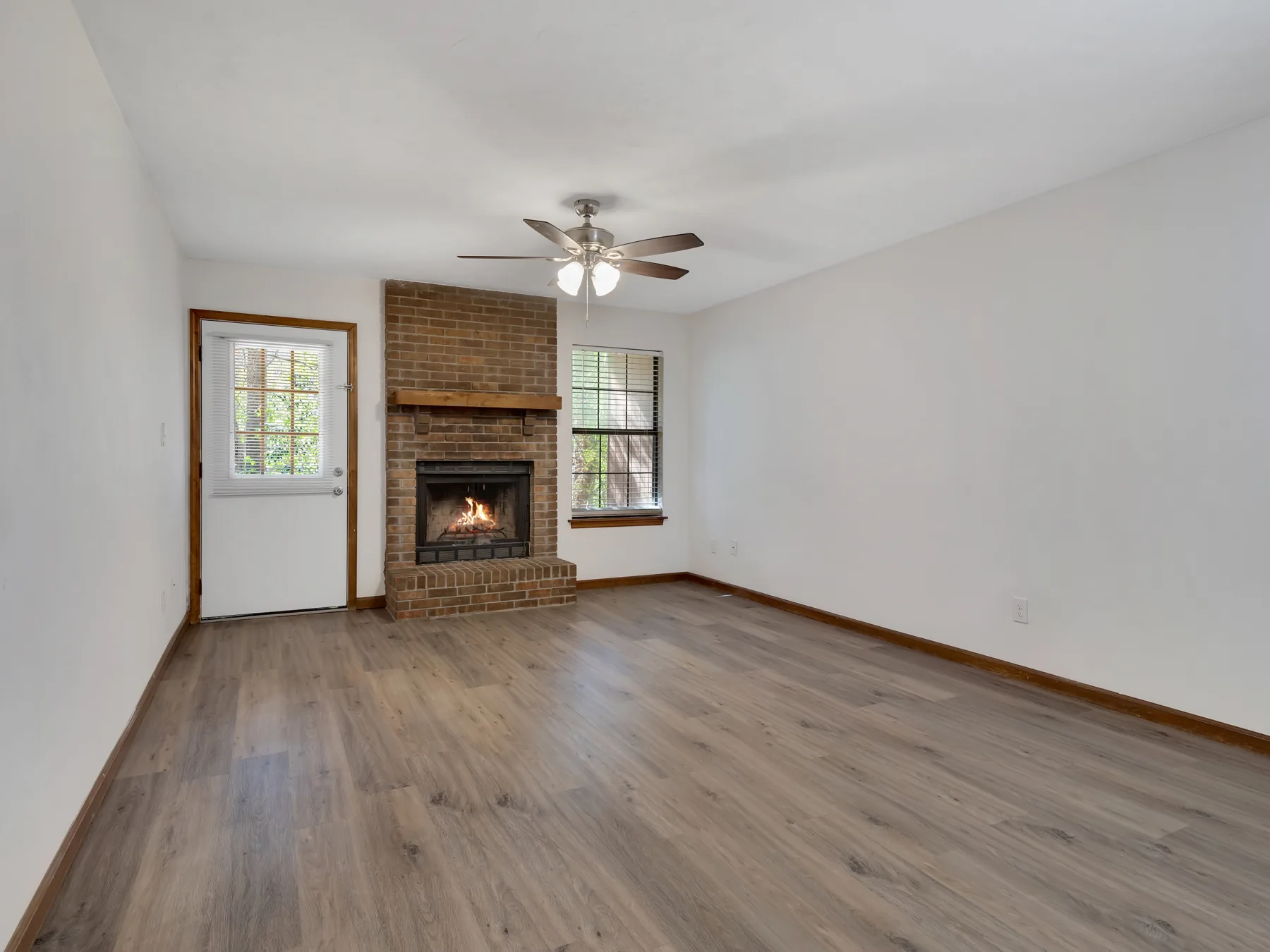 Living room with wood-burning brick fireplace, two windows and wood-style flooring at Castle Apartments, Tallahassee